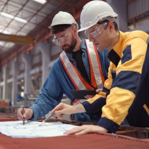 Team of engineers and architects working with blueprint at factory site. It is a massive new facility for making metal sheets as well as a transportation and distribution warehouse. Team of engineers and architects working with blueprint at factory site. It is a massive new facility for making metal sheets as well as a transportation and distribution warehouse.
